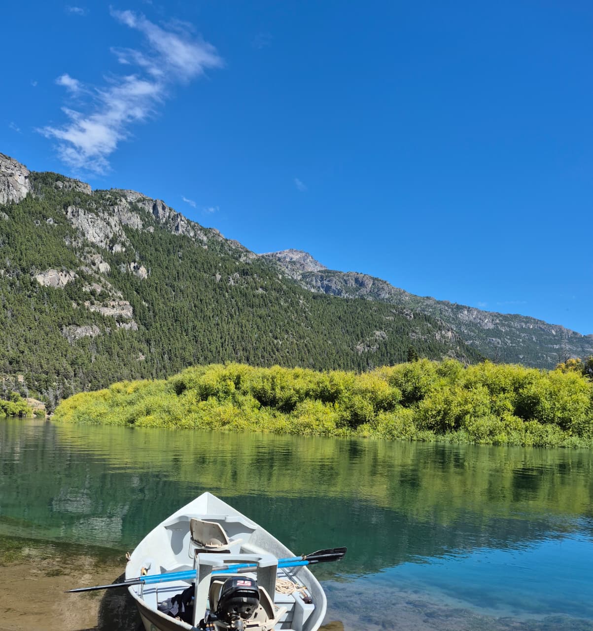 Barco de pesca em lago cristalino com montanhas ao fundo